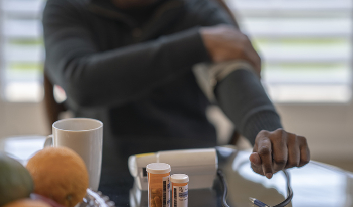 Mature man uses a home medical device to check his blood pressure while sitting at his kitchen table. 