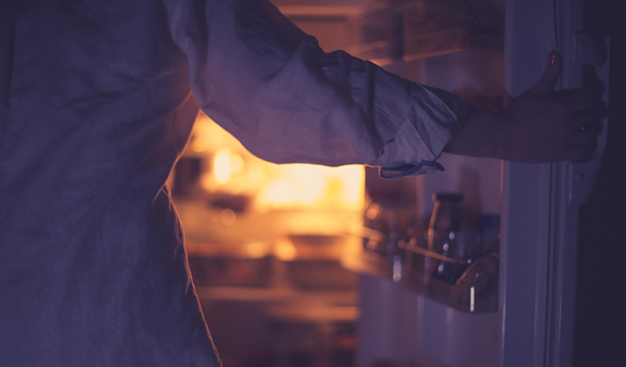 Close-up of woman holding the open refrigerator door during the night 