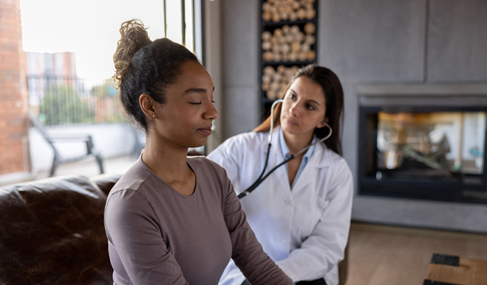 Latin American female doctor performing a medical exam to a patient at home - healthcare and medicine concepts